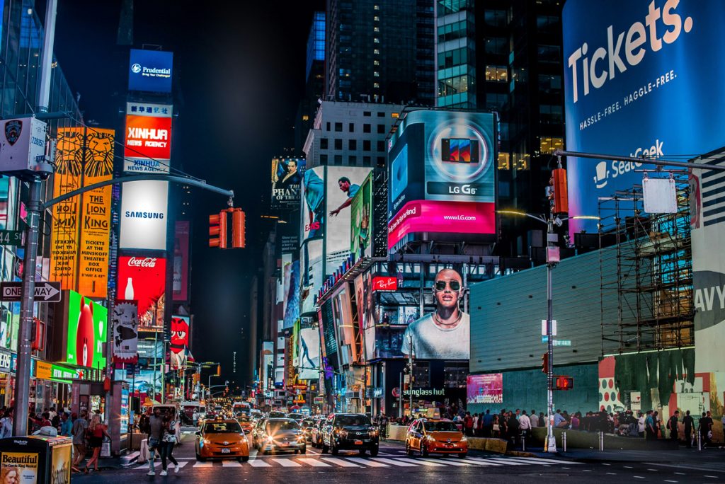 mídia externa na Times Square à noite com painéis digitais e táxis em movimento
