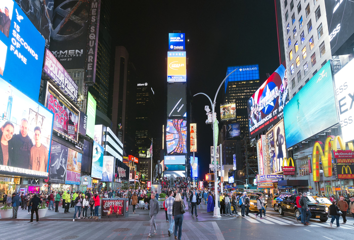 Grande concentração de painéis de mídia OOH em uma área urbana movimentada, com outdoors digitais, letreiros luminosos e alto fluxo de pessoas e veículos.