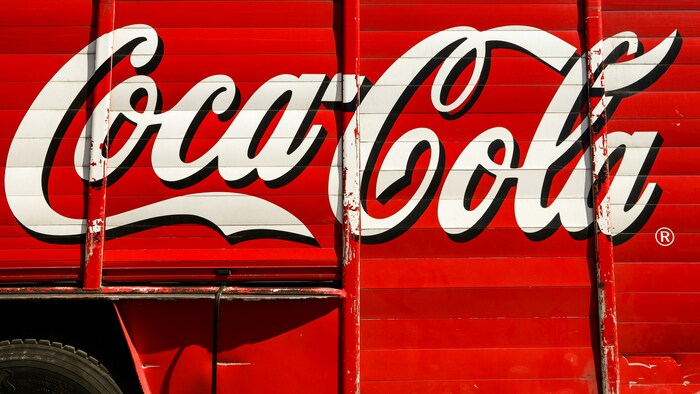 Painel lateral de caminhão com o logotipo tradicional da Coca-Cola em vermelho e branco, demonstrando como a repetição visual em grande escala aumenta o impacto visual, a memorização visual e o posicionamento de marca; um símbolo de comunicação visual consistente que sustenta uma imagem de marca forte ao longo das décadas. 